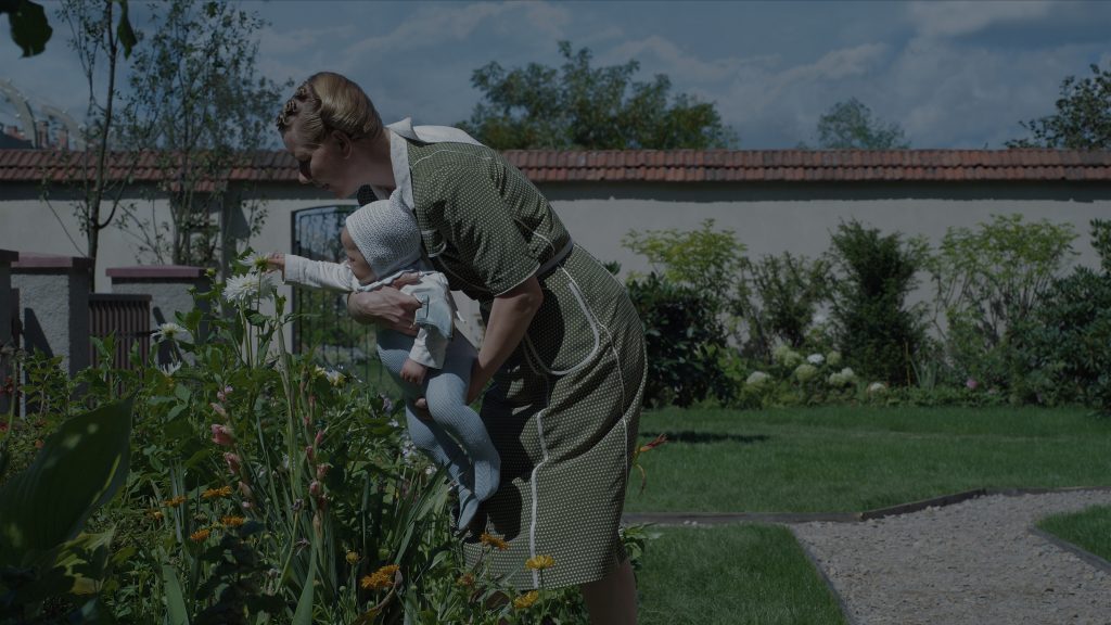 Photographie de Hedwig Höss (jouée par une Sandra Hüller absolument inquiétante), jouissant des plaisirs simples, dans son jardin, ici en présentant des fleurs à son nourrisson - © Bac Films / DR